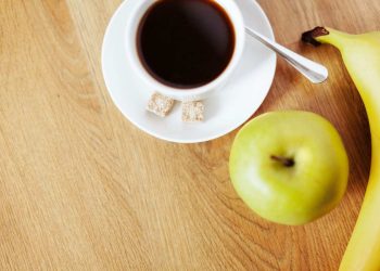 Cup of coffee with green apple and banana on wooden table.