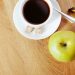 Cup of coffee with green apple and banana on wooden table.
