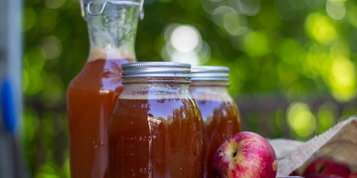 Homemade apple cider in glass jars with fresh apples nearby.