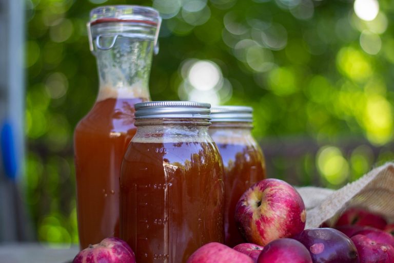 Homemade apple cider in glass jars with fresh apples nearby.