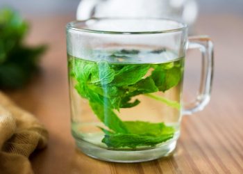 Fresh mint leaves steeping in a glass of herbal tea.