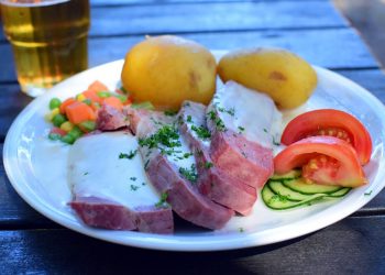 Roast beef with creamy sauce, potatoes, and fresh vegetables on a plate.