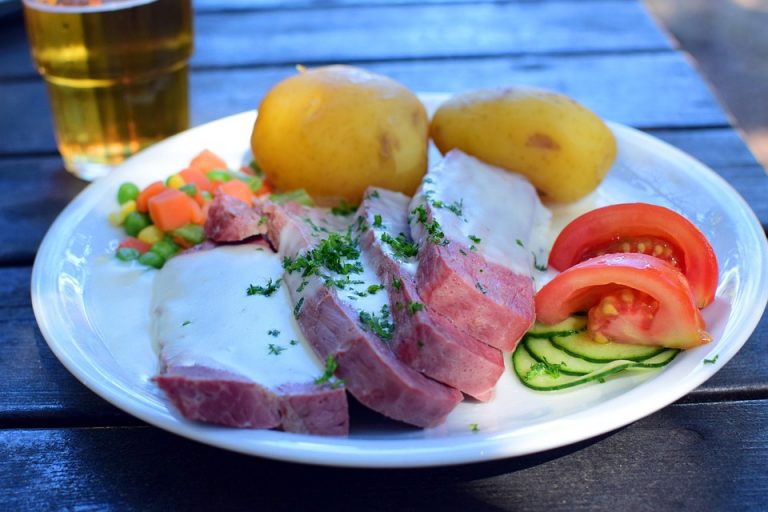 Roast beef with creamy sauce, potatoes, and fresh vegetables on a plate.