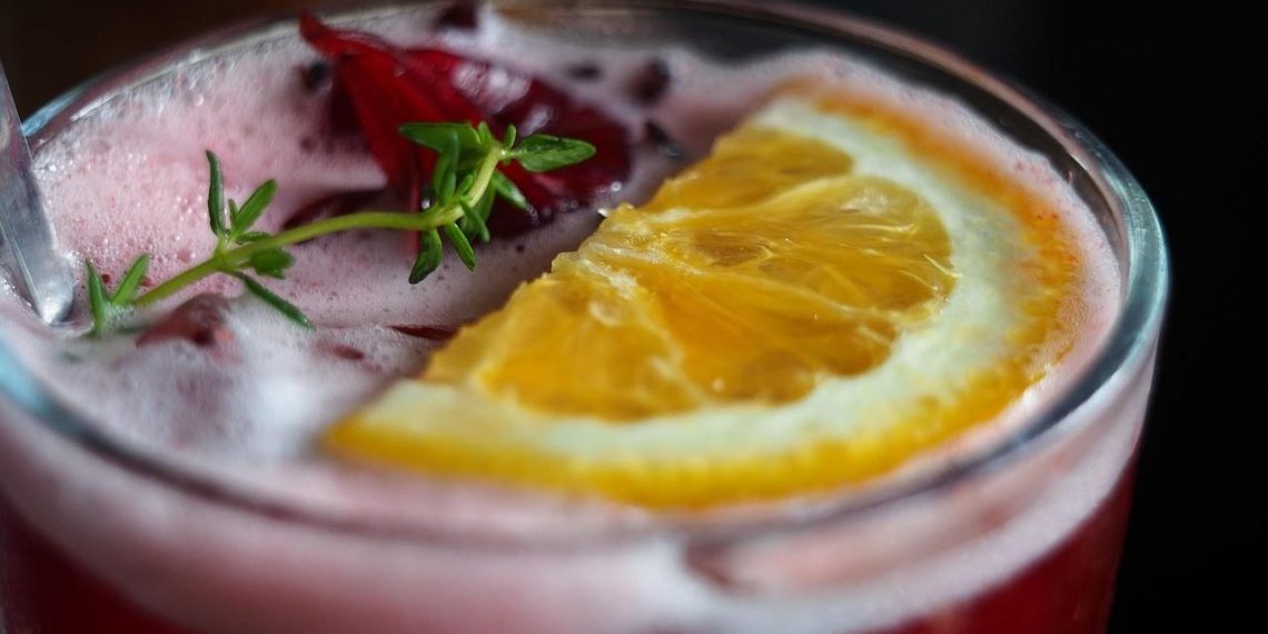 Refreshing hibiscus cocktail with orange slice garnish.
