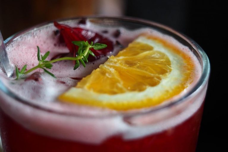 Refreshing hibiscus cocktail with orange slice garnish.