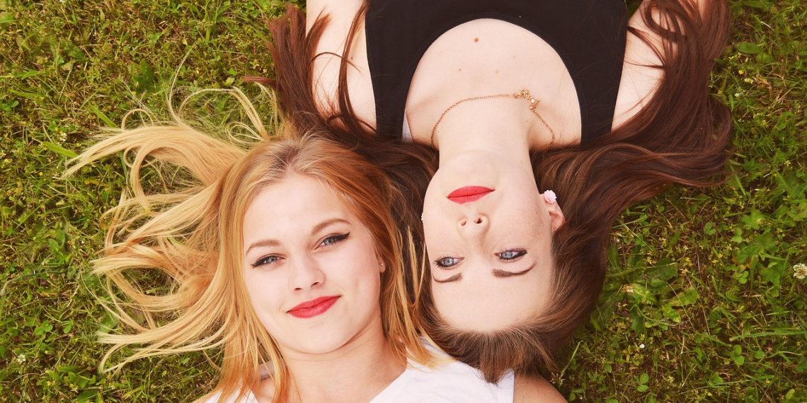 Two smiling women lying on grass, heads together.
