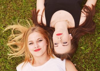 Two smiling women lying on grass, heads together.