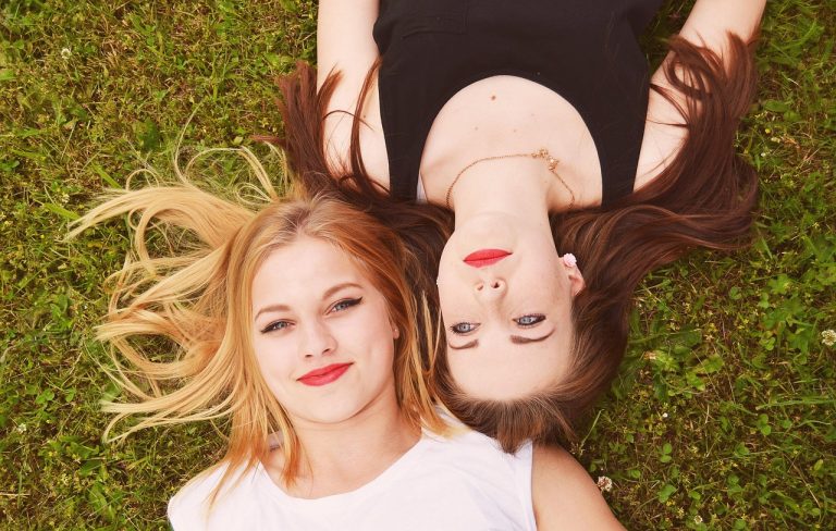 Two smiling women lying on grass, heads together.