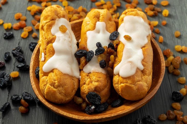 Cream eclairs topped with raisins on a wooden plate.