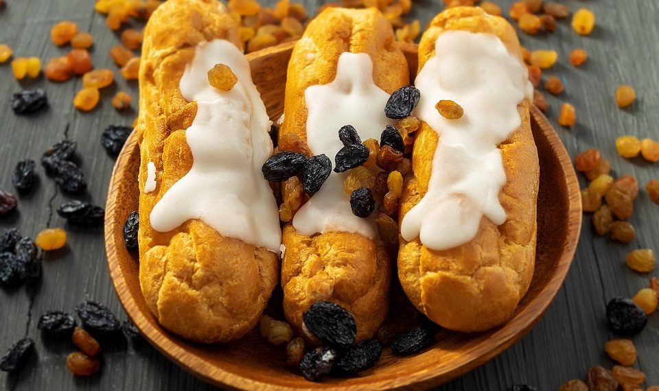 Cream eclairs topped with raisins on a wooden plate.