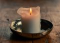 Rustic white candle burning on wooden table.