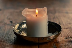Rustic white candle burning on wooden table.