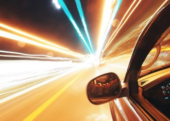 Car speeding on a highway at night with light trails.