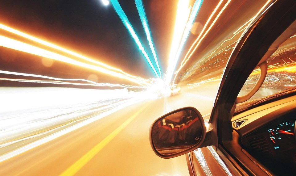 Car speeding on a highway at night with light trails.