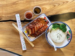Sliced duck with rice and broccoli, soy sauce, and chopsticks on a wooden table.