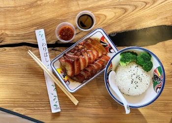 Sliced duck with rice and broccoli, soy sauce, and chopsticks on a wooden table.