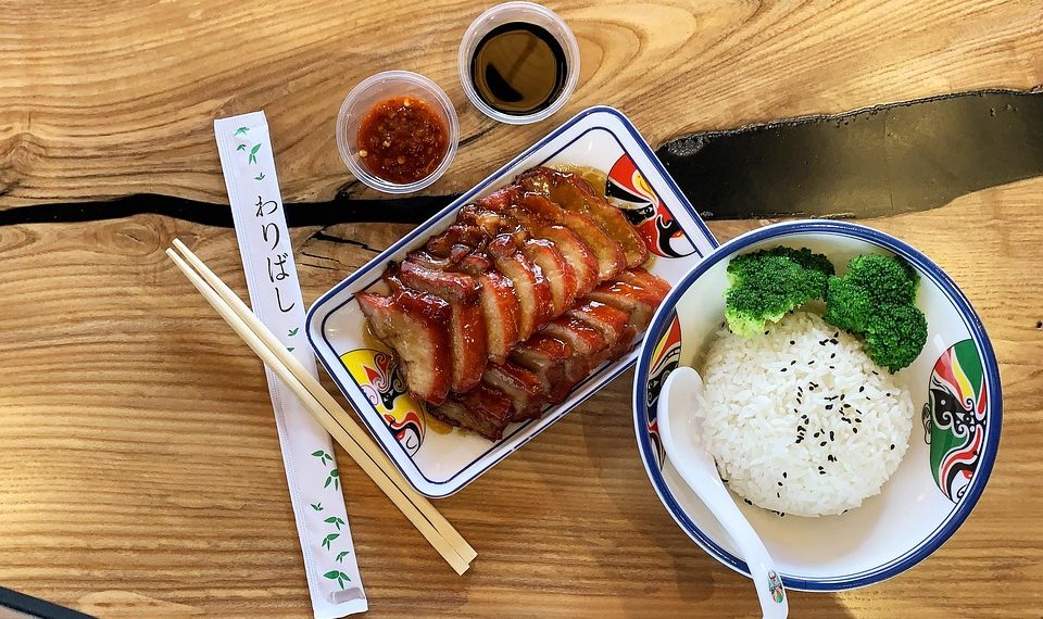 Sliced duck with rice and broccoli, soy sauce, and chopsticks on a wooden table.