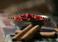 Bowl of pink peppercorns and cinnamon sticks on a table.