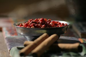 Bowl of pink peppercorns and cinnamon sticks on a table.