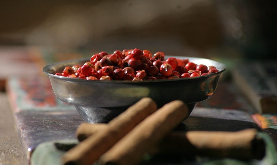 Bowl of pink peppercorns and cinnamon sticks on a table.