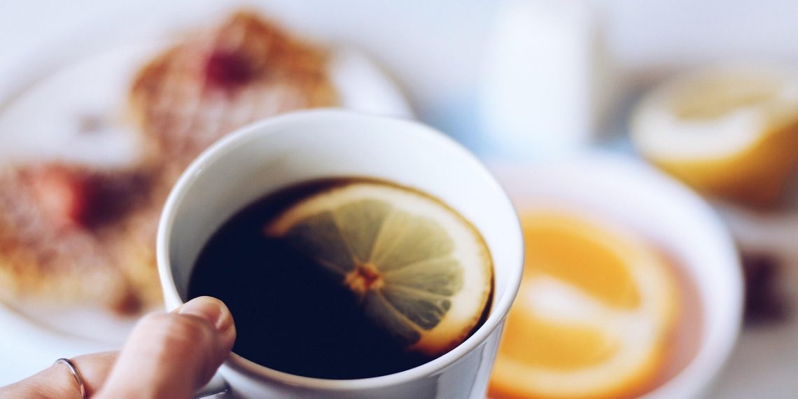 Hand holding a coffee cup with a lemon slice.