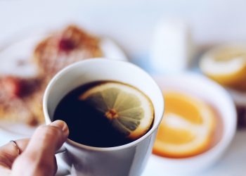 Hand holding a coffee cup with a lemon slice.