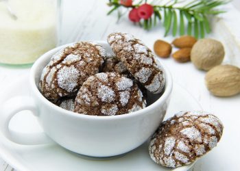 Chocolate crinkle cookies in a teacup with almonds nearby.