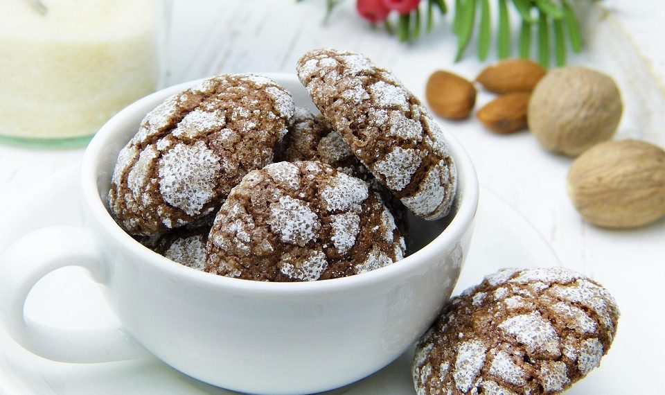 Chocolate crinkle cookies in a teacup with almonds nearby.