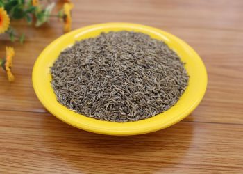 Cumin seeds piled on a bright yellow plate on a wooden table.