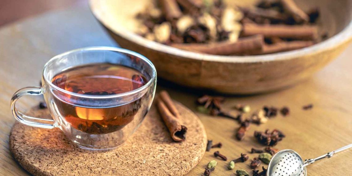 Herbal chai tea with spices in a glass cup on a cork coaster.