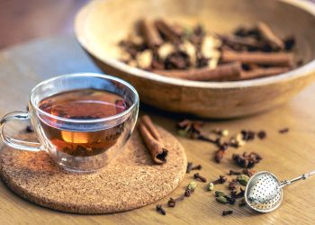 Herbal chai tea with spices in a glass cup on a cork coaster.