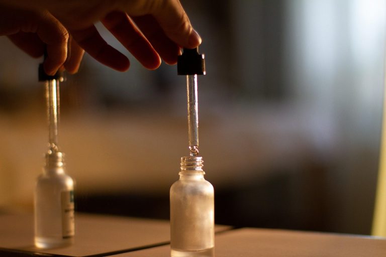 Hand using a dropper to dispense liquid into a small glass bottle.