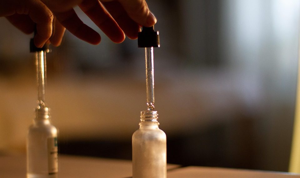 Hand using a dropper to dispense liquid into a small glass bottle.