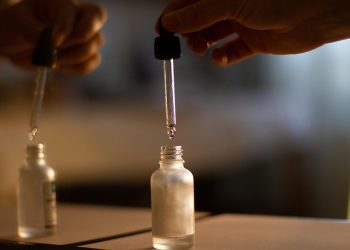 Hand using dropper to transfer liquid into small glass bottle.