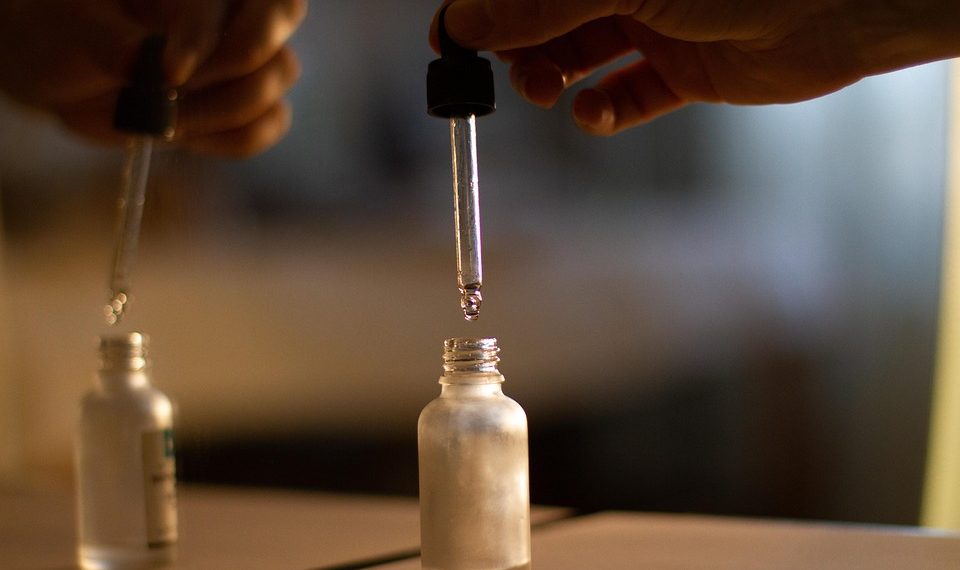 Hand using dropper to transfer liquid into small glass bottle.