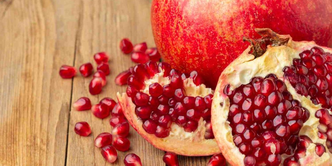 Pomegranate with scattered seeds on wooden surface.