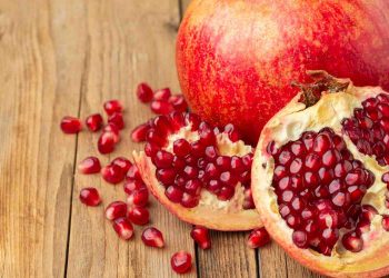 Pomegranate with scattered seeds on wooden surface.