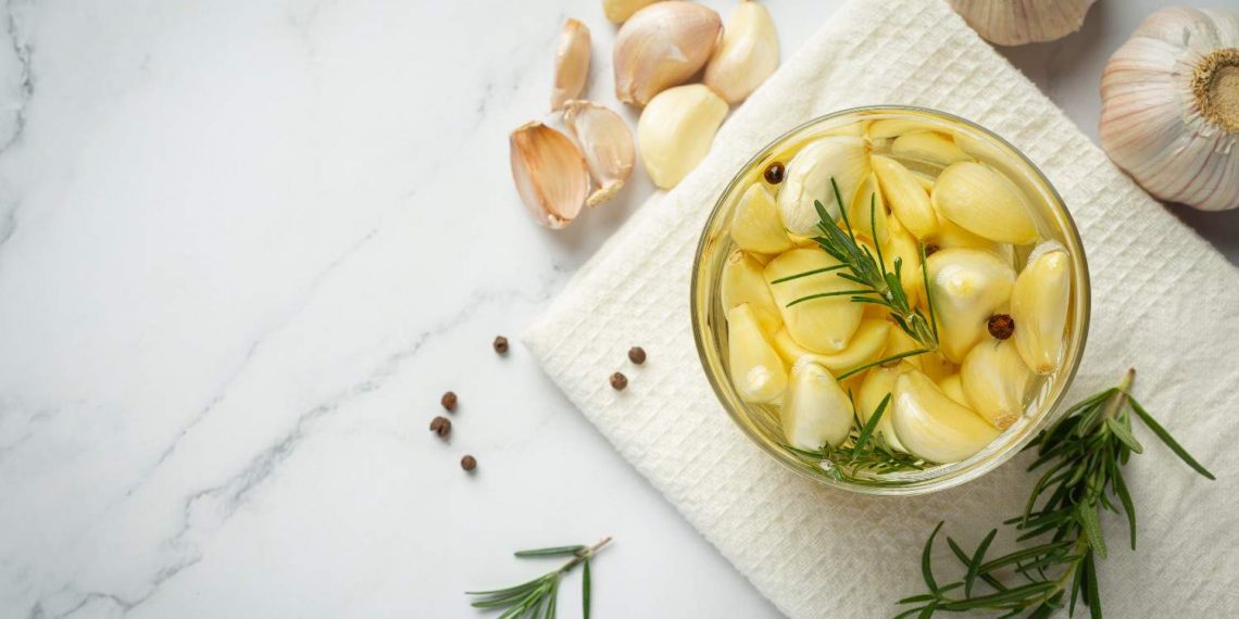 Garlic cloves with rosemary in a jar on a white cloth.