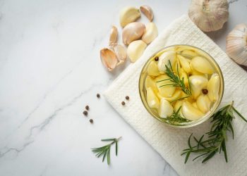 Garlic cloves with rosemary in a jar on a white cloth.