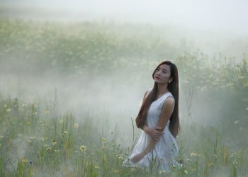 Woman in white dress kneeling in a foggy, floral meadow.