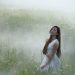 Woman in white dress kneeling in a foggy, floral meadow.