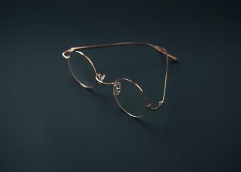 Round rose gold eyeglasses on a dark background.