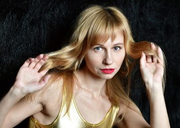 Blonde woman with red lipstick holding her long hair.