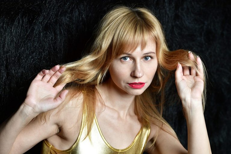 Blonde woman with red lipstick holding her long hair.