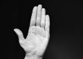 Raised hand against black background, palm open.