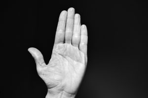 Raised hand against black background, palm open.