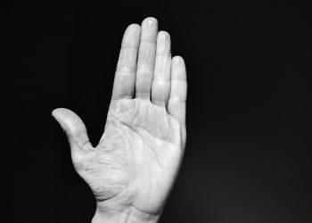Raised hand against black background, palm open.