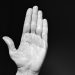 Raised hand against black background, palm open.