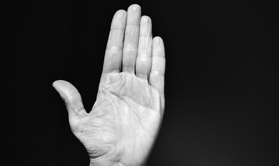 Raised hand against black background, palm open.
