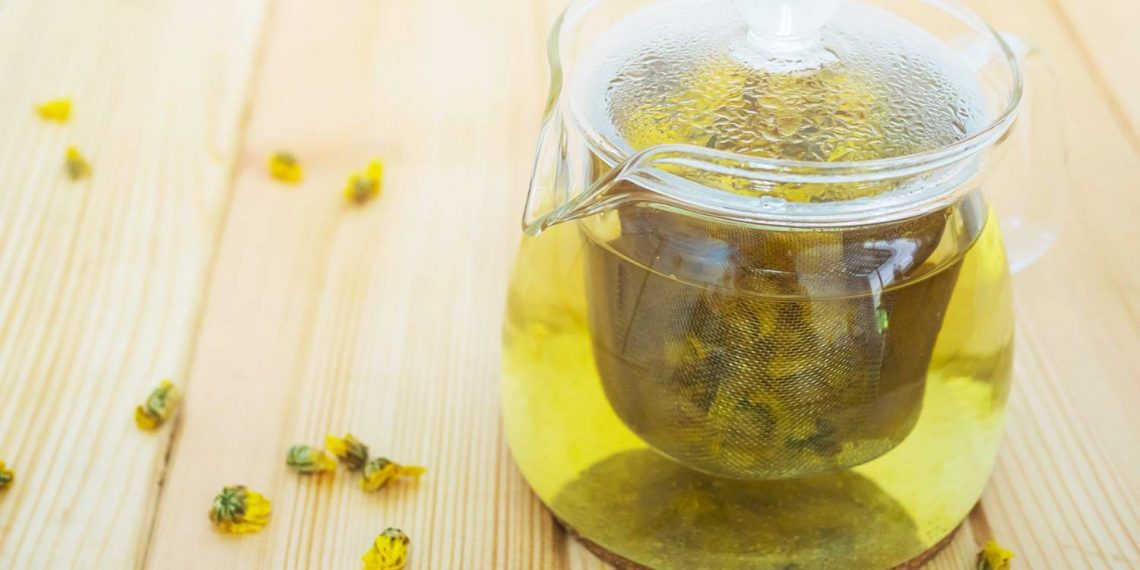 Glass teapot brewing chrysanthemum tea on wooden table.